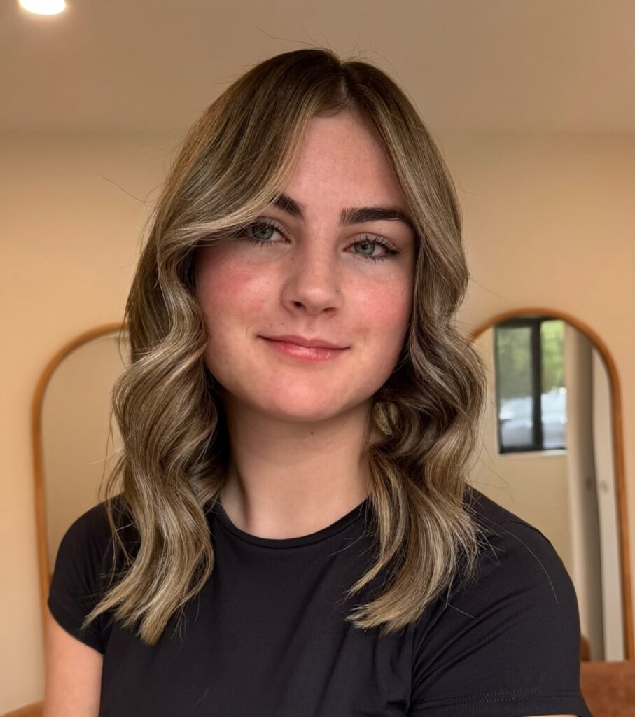 A woman with medium length ash blonde hair styled in soft defined waves with a middle part.