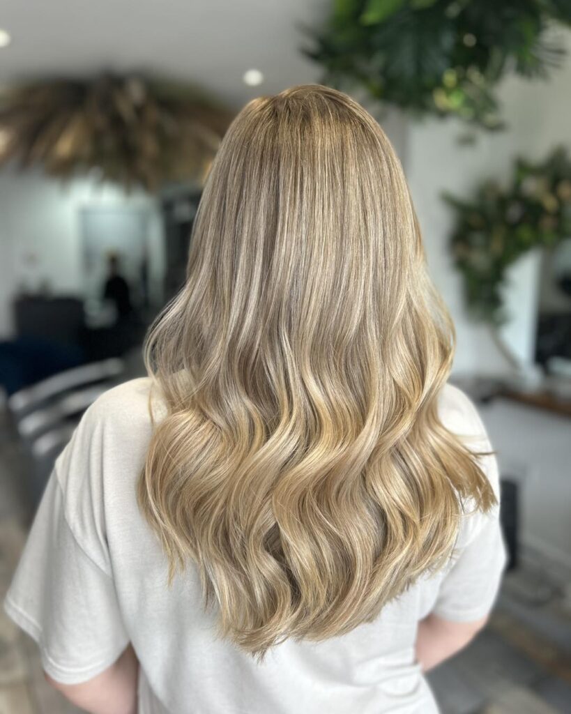 The back view of a woman with medium length sandy blonde hair styled in soft uniform waves.