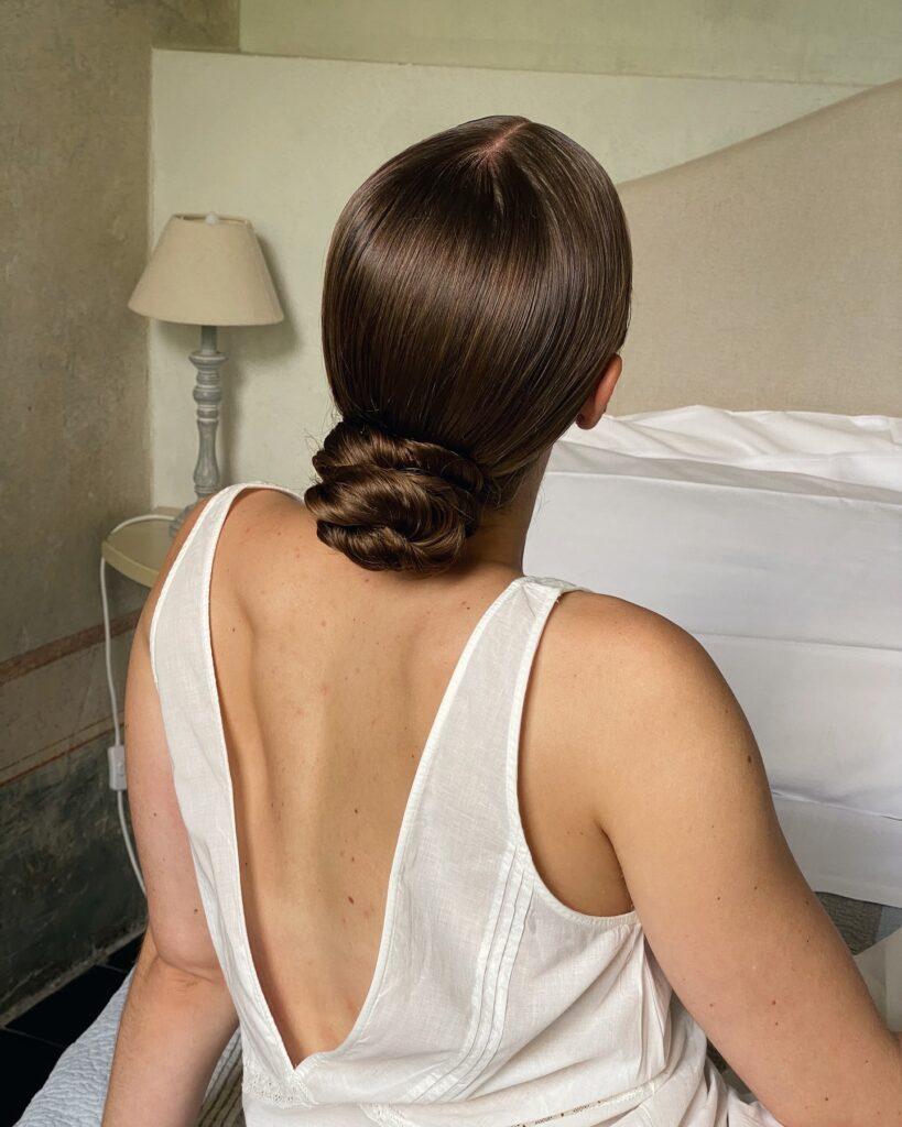 Glossy low chignon with a smooth rounded shape at the nape.