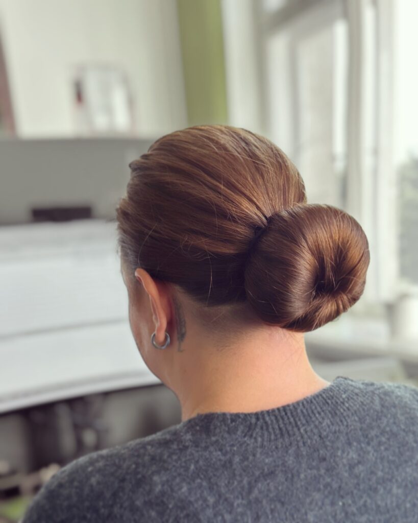 Dark hair styled into a sleek donut shaped low bun with a smooth finish.