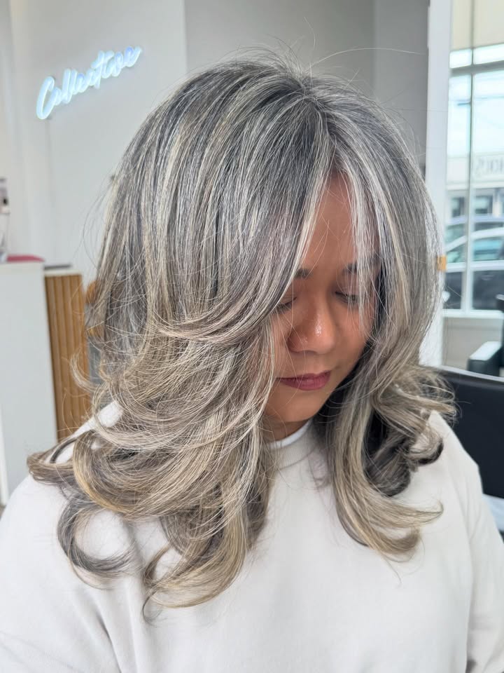 Long silver layered hair with curtain bangs and voluminous soft curls.