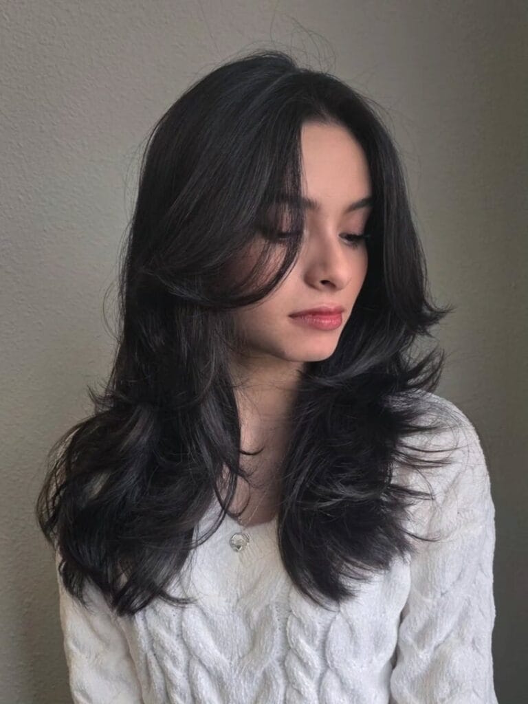 A woman with long black hair styled in voluminous butterfly layers and flicked out face framing bangs.