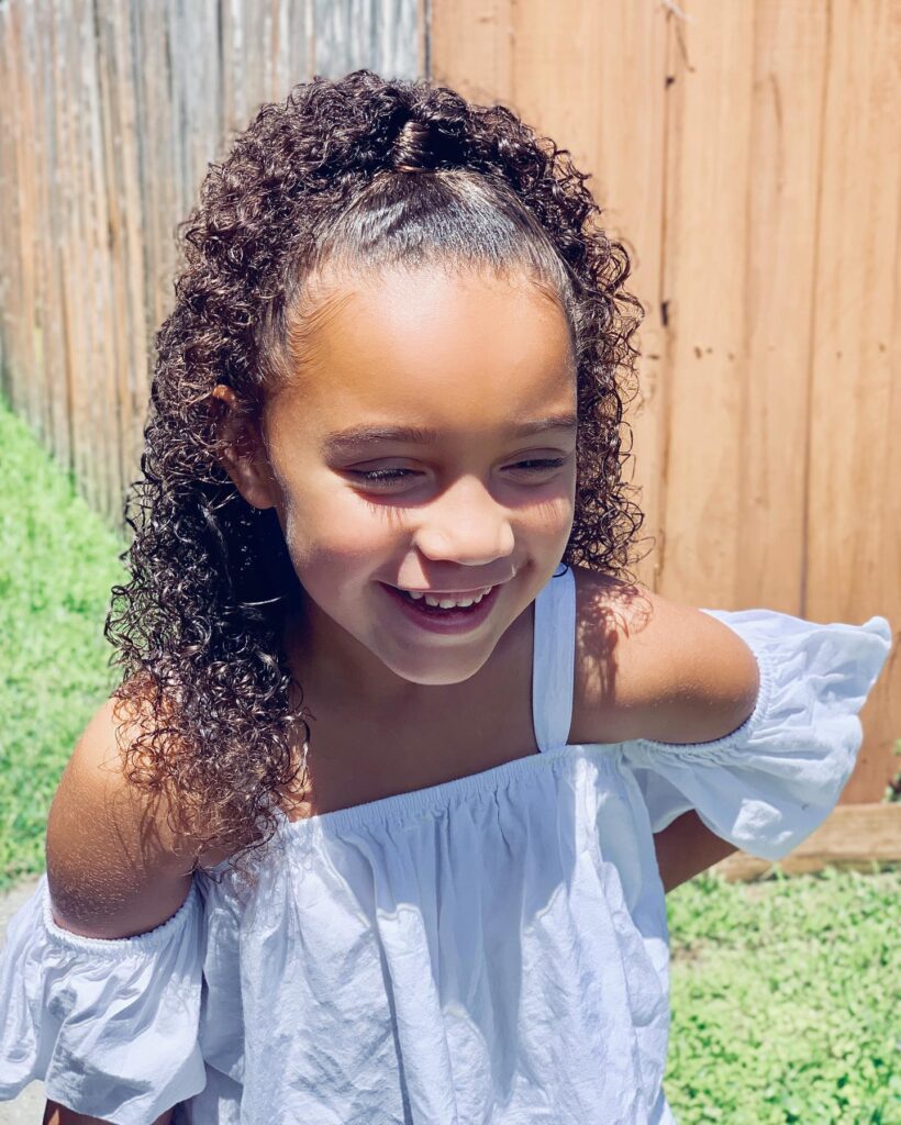 A young girl with a sleek high ponytail and loose dark ringlets cascading down her back.