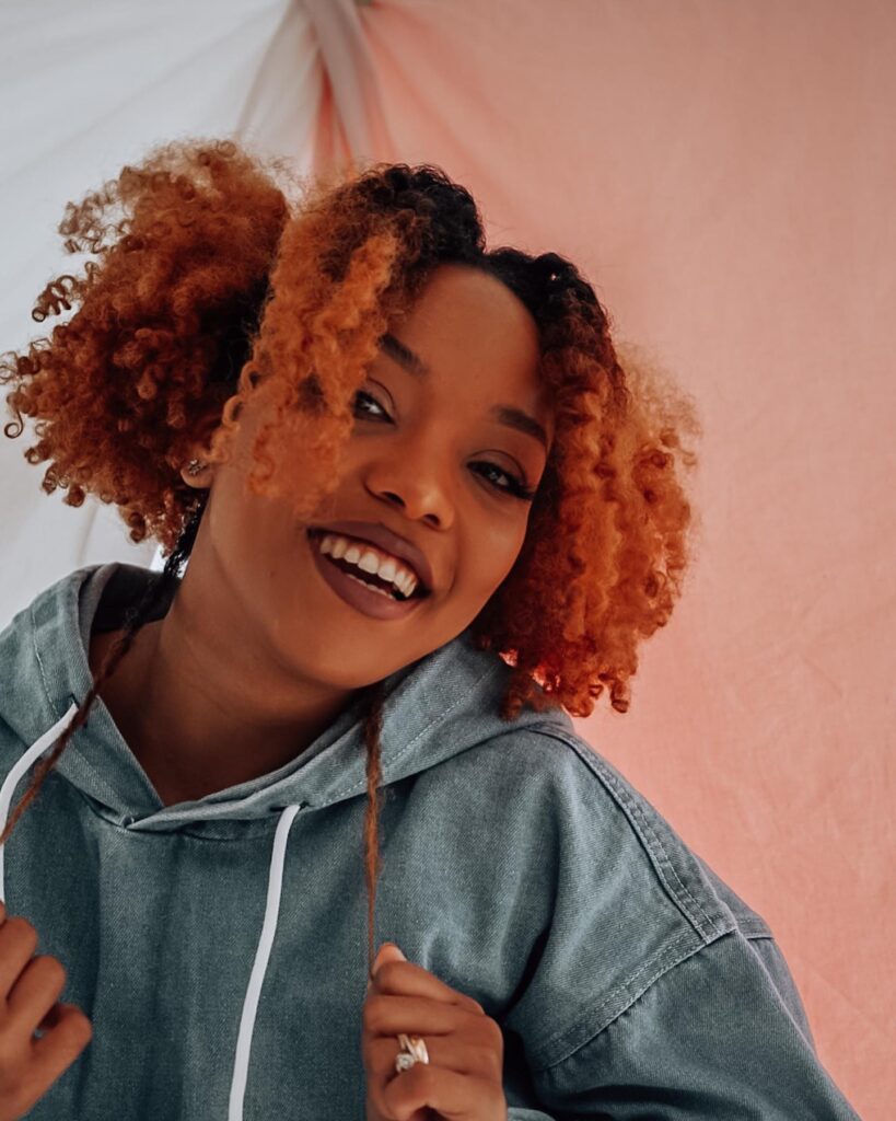 A woman smiling while showing off her voluminous black and honey-orange ombré curly hair.