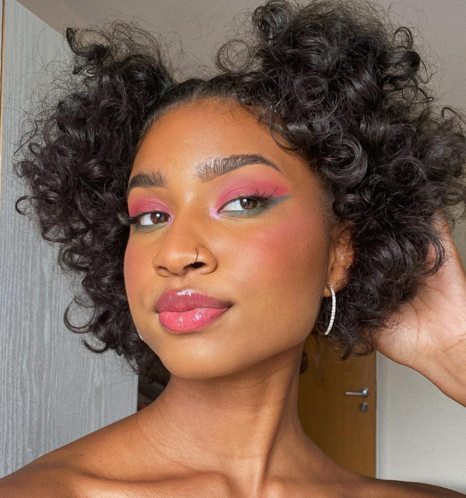 A woman with shoulder-length dark curly hair styled into two half-up space buns with soft voluminous ringlets.