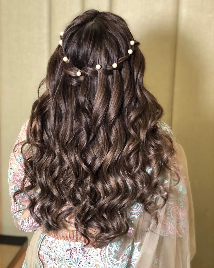 A back view of long, chocolate brown hair styled in a waterfall braid accented with delicate pearl beads and flowing into bouncy waves.