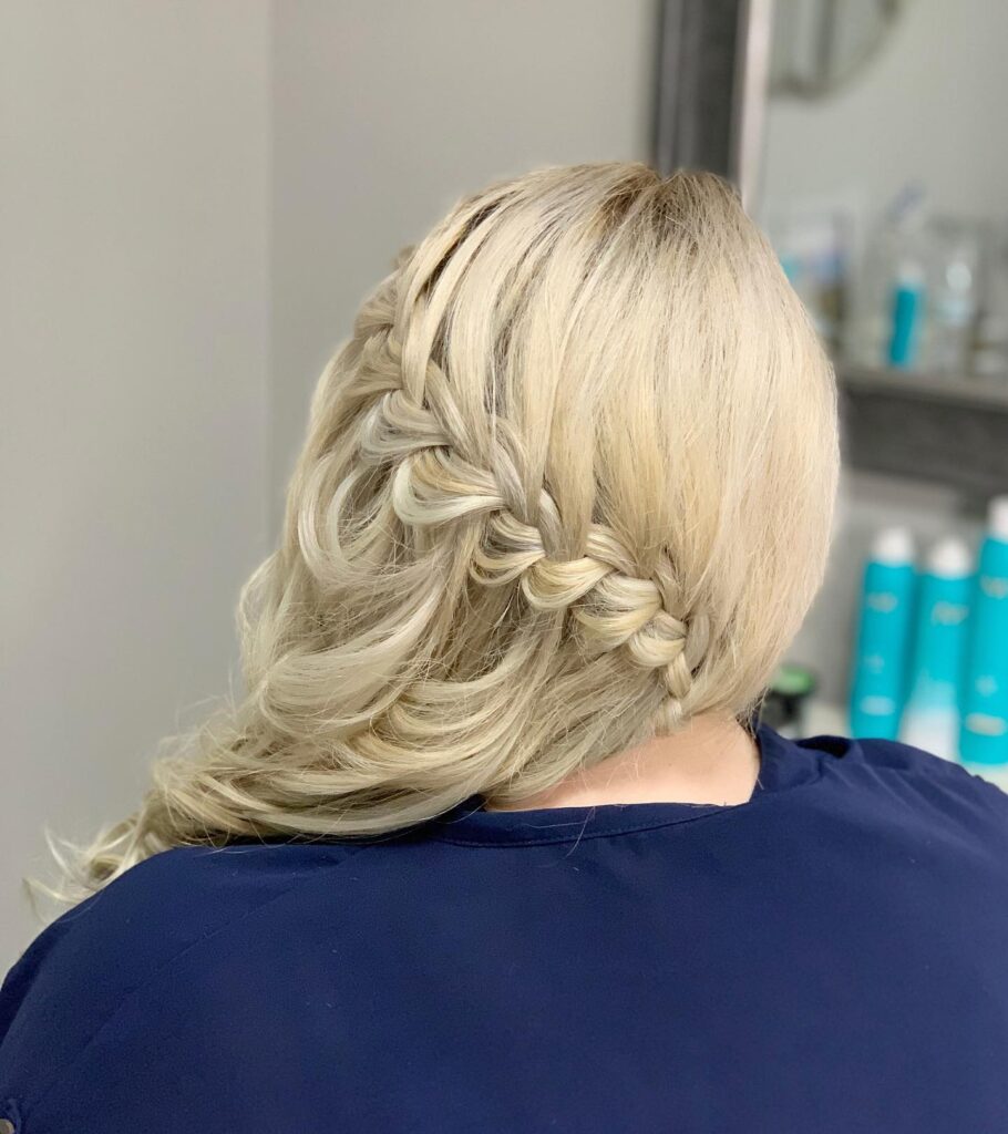 A side view of a woman with platinum blonde hair featuring a thick diagonal waterfall braid that transitions into soft, flowing waves.