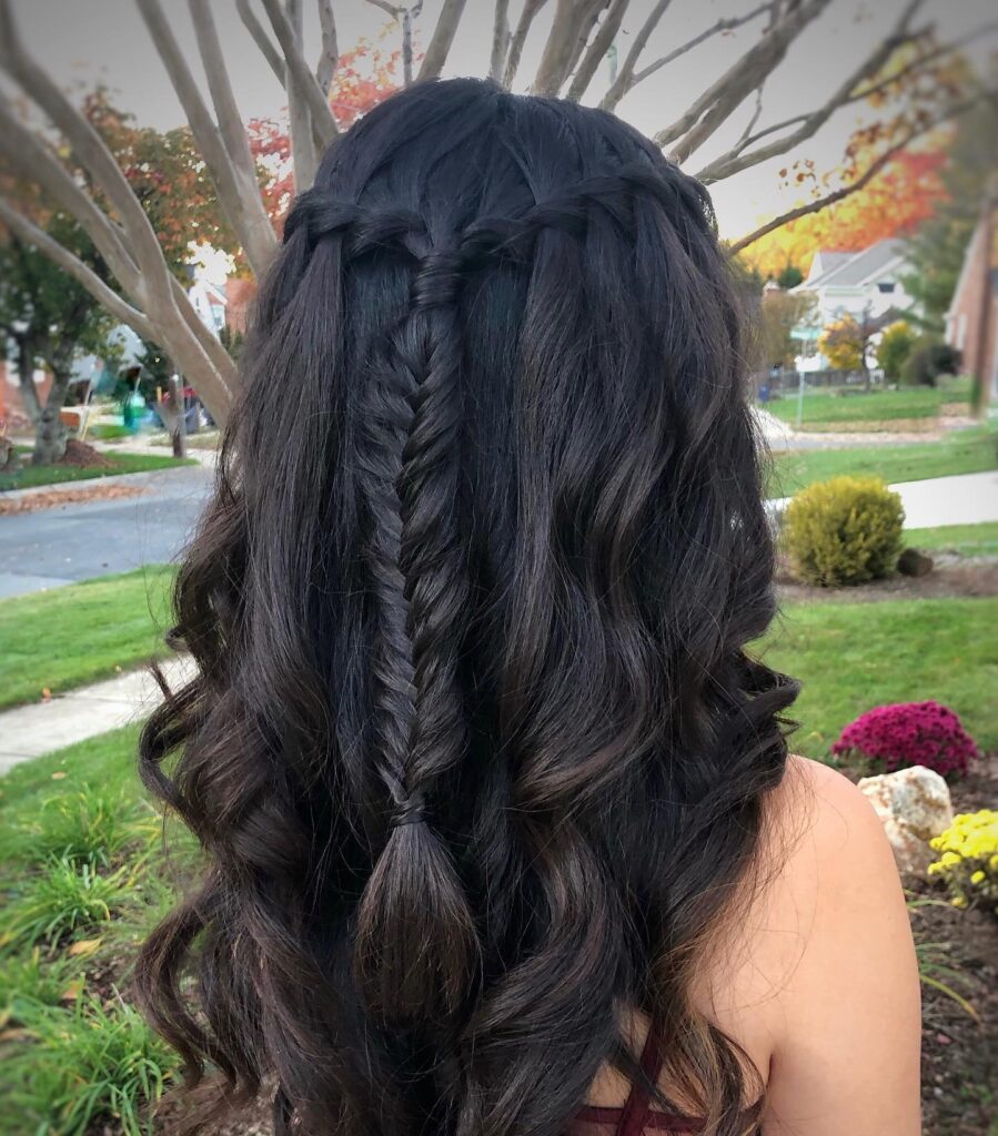 A back view of long black hair styled with a waterfall braid that merges into a central fishtail braid over loose wavy layers.