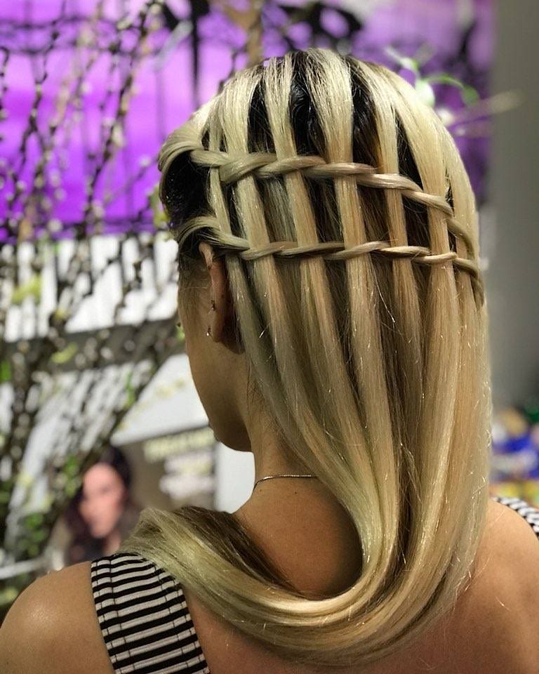 A back view of a woman with blonde hair and dark roots featuring a structured double waterfall braid that creates a ladder-like geometric pattern.