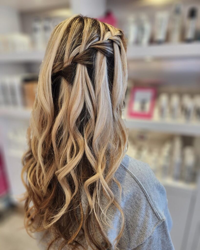 A back view of long hair with high-contrast blonde highlights styled in a chunky diagonal waterfall braid and loose waves.