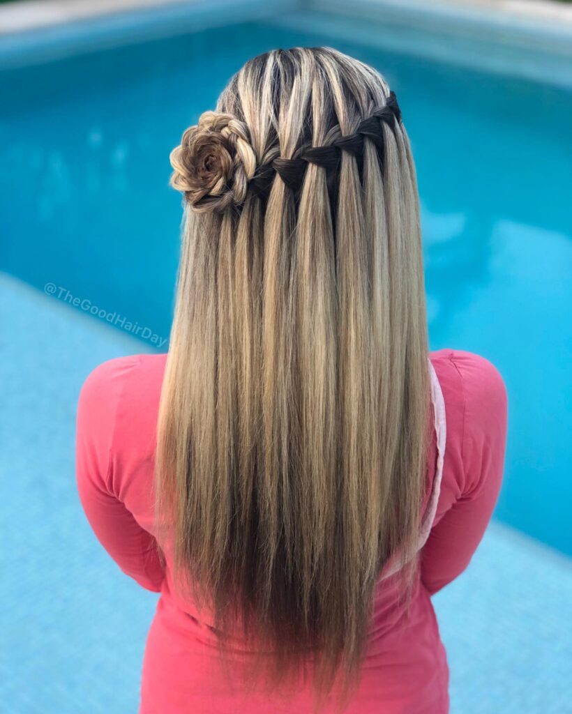 A back view of long, straight, ash blonde hair featuring a waterfall braid that ends in a beautiful hair rosette on one side.