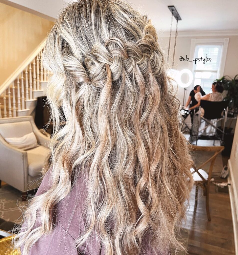 A back view of long, ash blonde hair with beachy waves and a thick chunky waterfall braid across the crown.