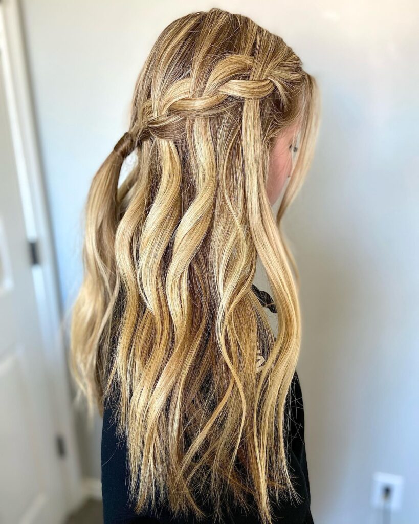 A side profile of a woman with long honey-blonde wavy hair styled in a thick horizontal waterfall braid.