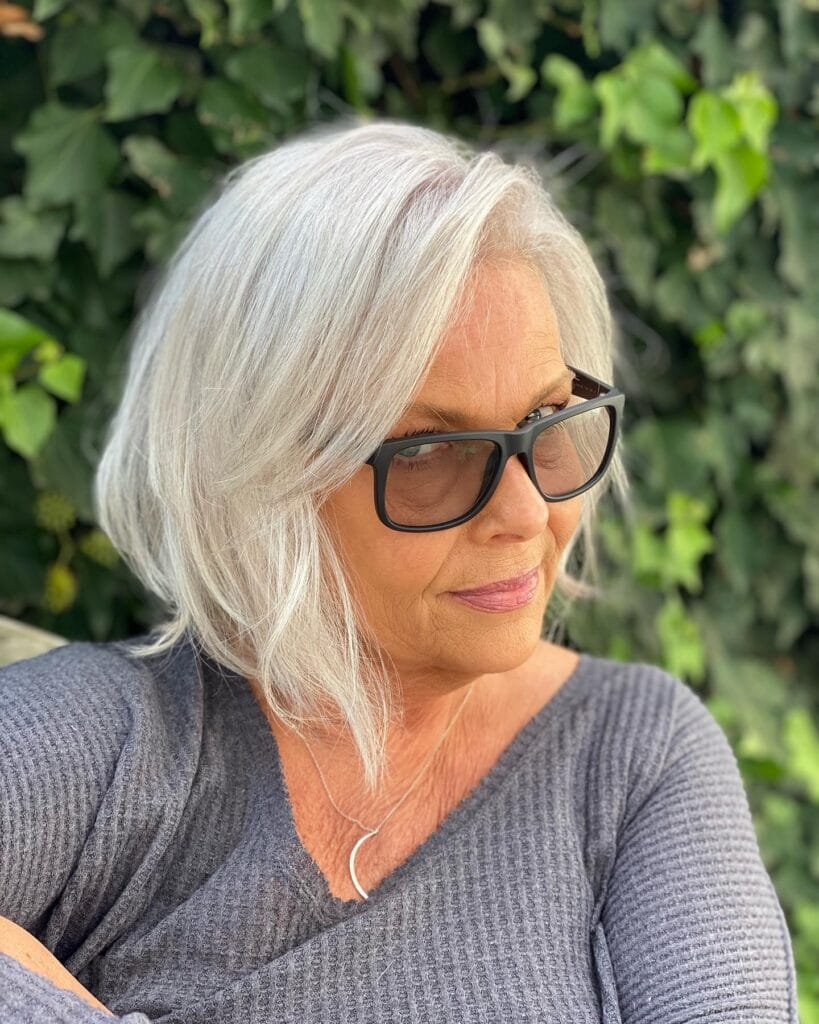 A woman with a bright white platinum angled bob hairstyle featuring soft layers and a side part while wearing black glasses.