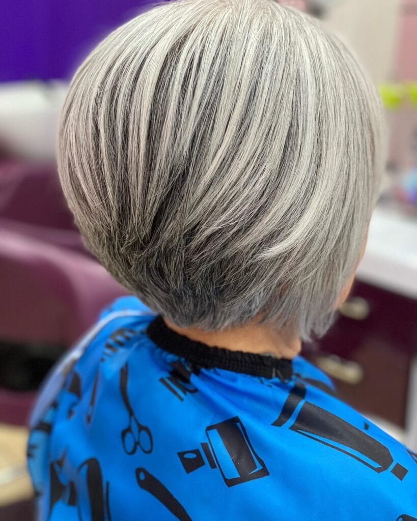 A close-up back view of a woman with a precision-stacked bob haircut featuring silver and charcoal gray highlights and a tapered nape.