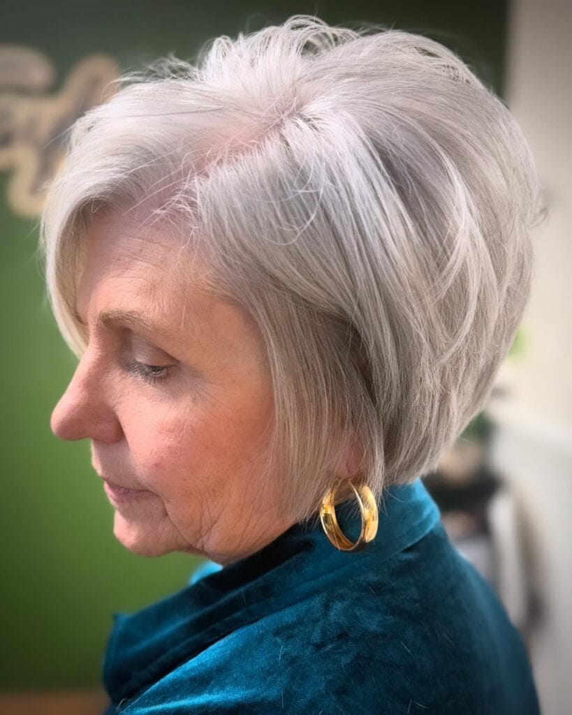 A side profile view of a woman with a tapered silver bob haircut featuring short layers at the nape and voluminous styling at the crown.