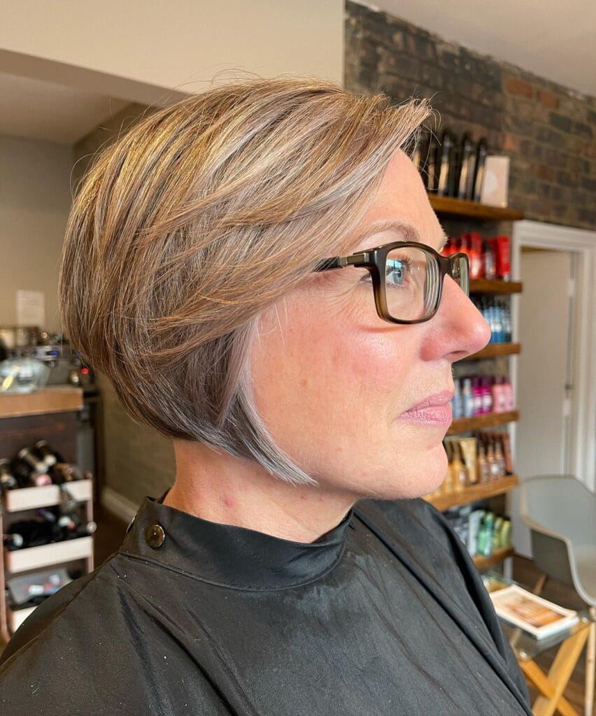 A side profile view of a woman with a stacked mushroom blonde bob hairstyle featuring graduated layers and a sharp jaw-length front.
