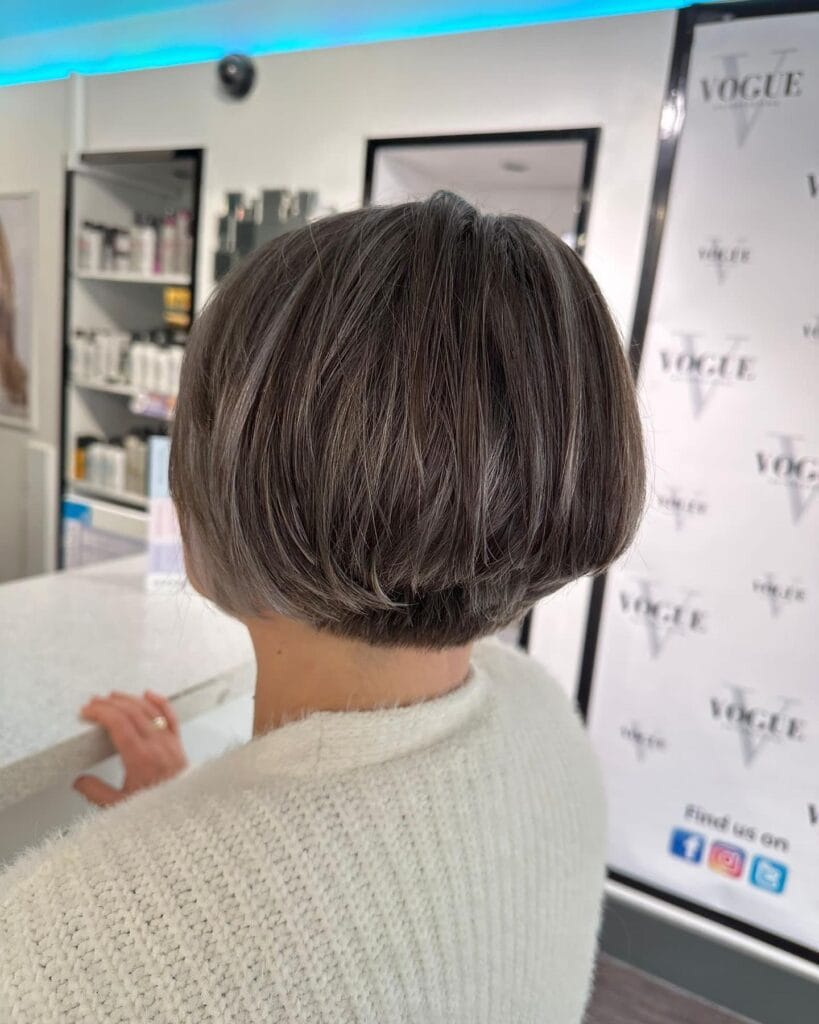 A back view of a woman with a sleek, rounded ash brown bob featuring silver highlights and a tapered nape.