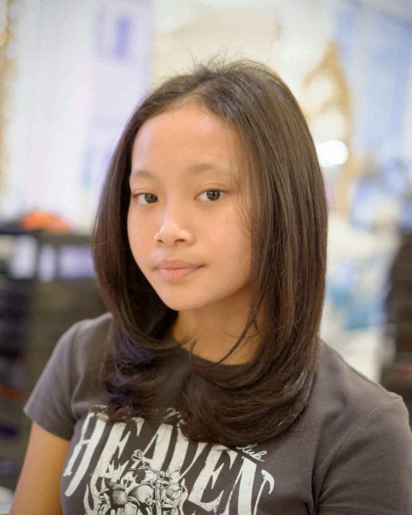 A young woman with shoulder-length dark brown hair styled with smooth face-framing layers.