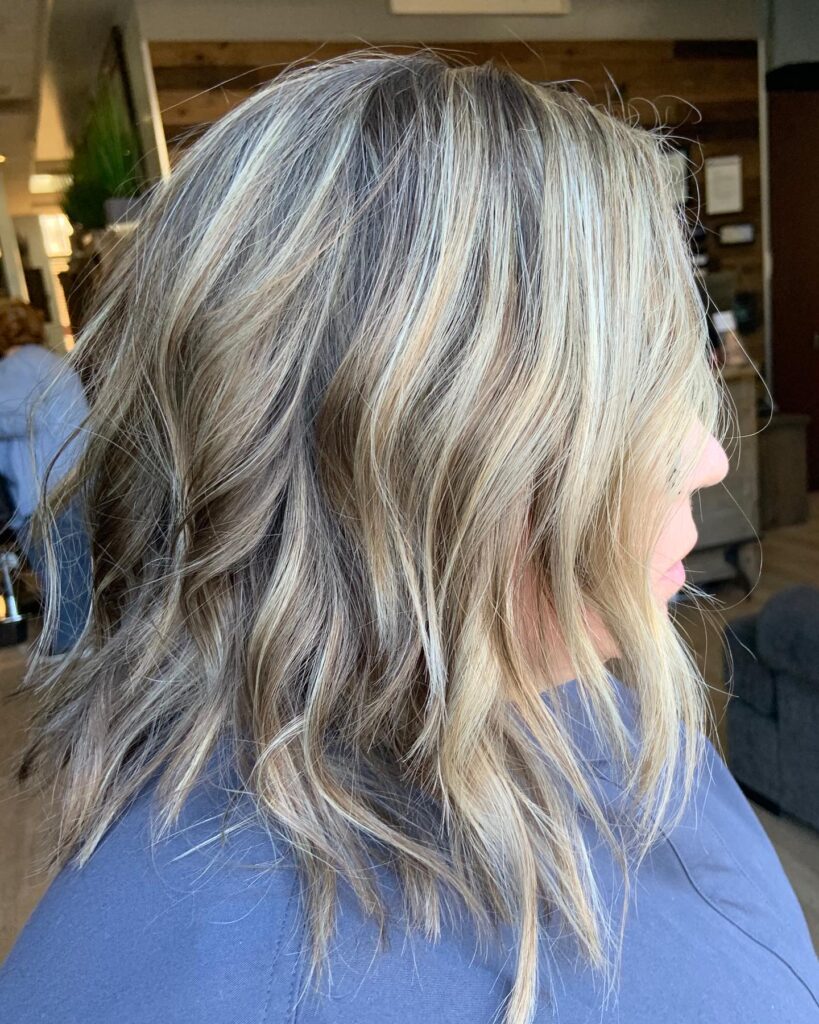 A medium-length wavy bob featuring chunky cool-toned blonde highlights and dimensional darker roots.