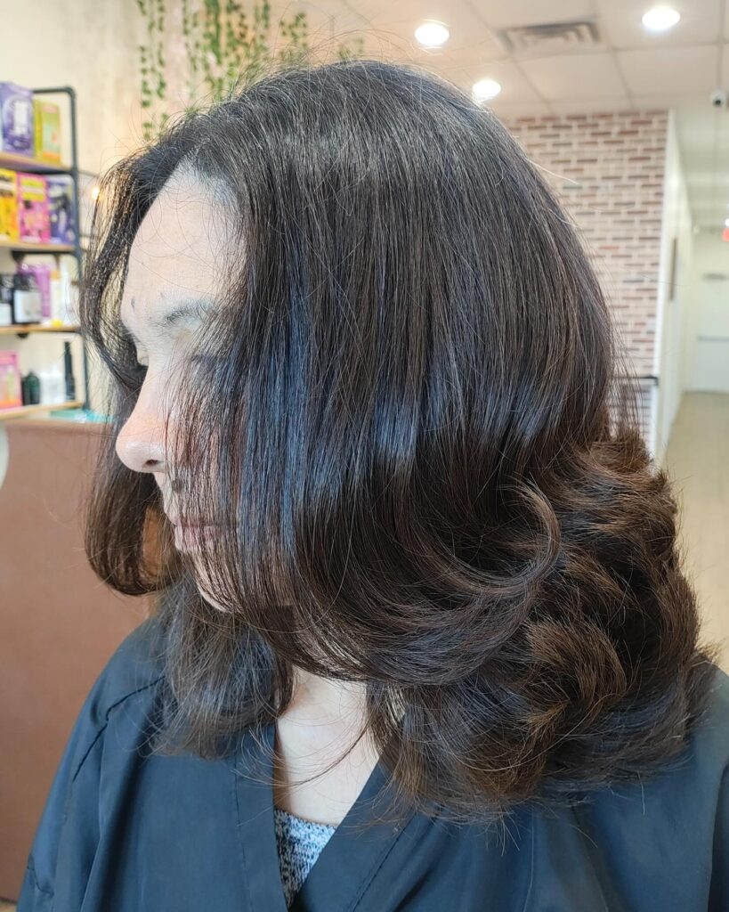 A woman with shiny medium dark brown hair styled with voluminous outward-flipped ends and long layers.