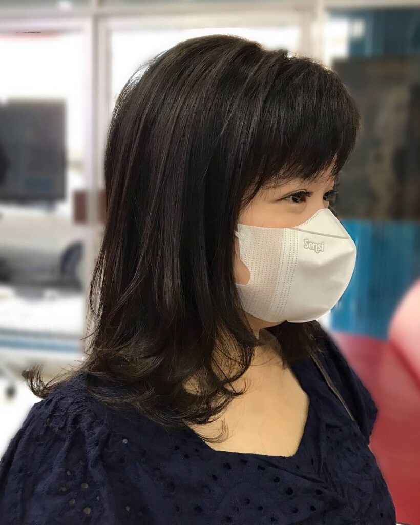 A woman with medium-length dark brown hair featuring full straight bangs and soft curled ends.