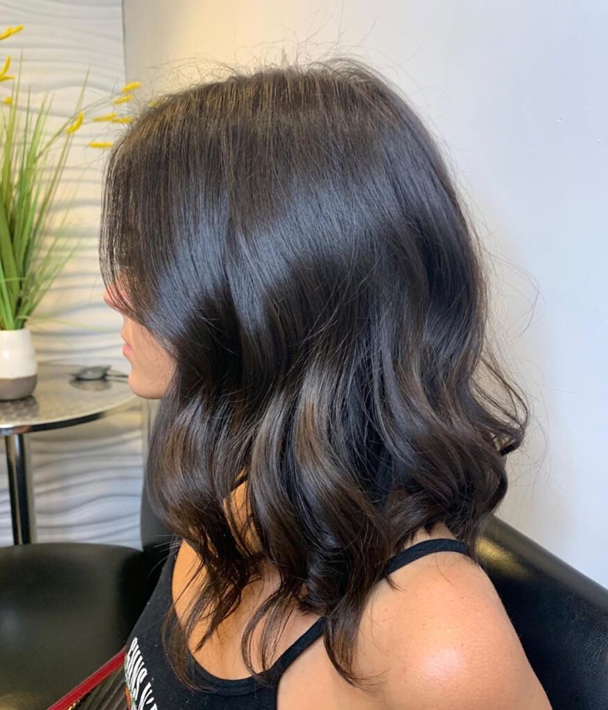 A side view of a woman with medium-length glossy espresso brown hair styled in large soft waves.
