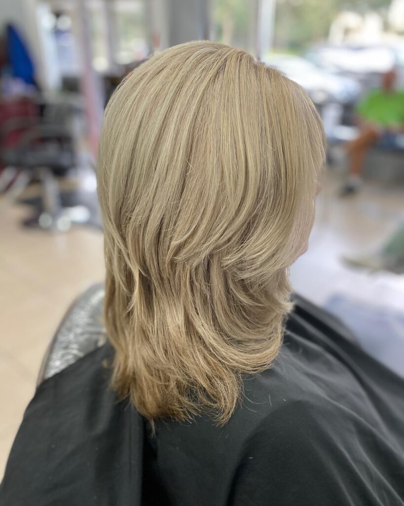 A side profile of a woman with medium-length sandy blonde hair featuring soft, feathered layers and a smooth finish.