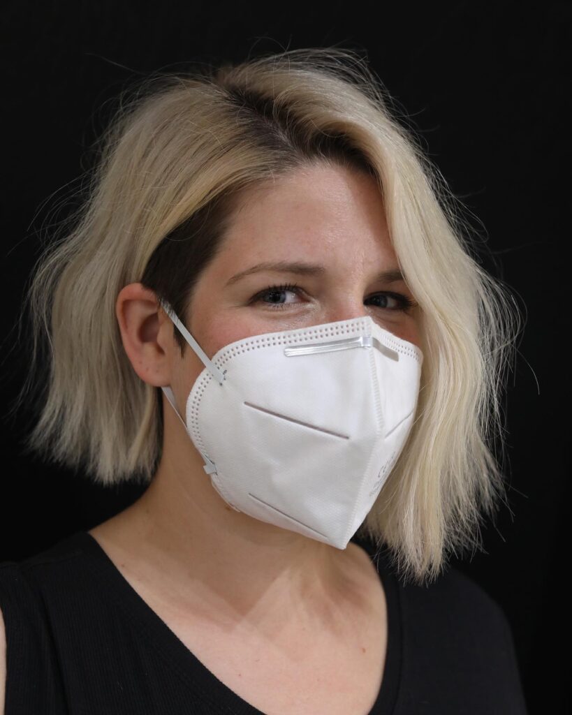 A person with a short, wavy blonde bob hairstyle that features a dark shaved undercut on one side, parted dramatically over to reveal the style.