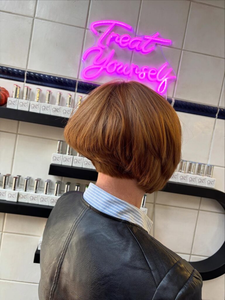 A rear view of a person with a stacked inverted bob hairstyle in a warm ginger brown color.