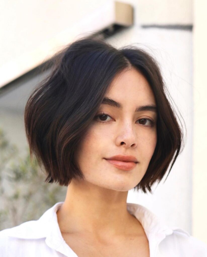 A woman with a jaw-length dark brunette French bob styled with a middle part and soft, voluminous waves.