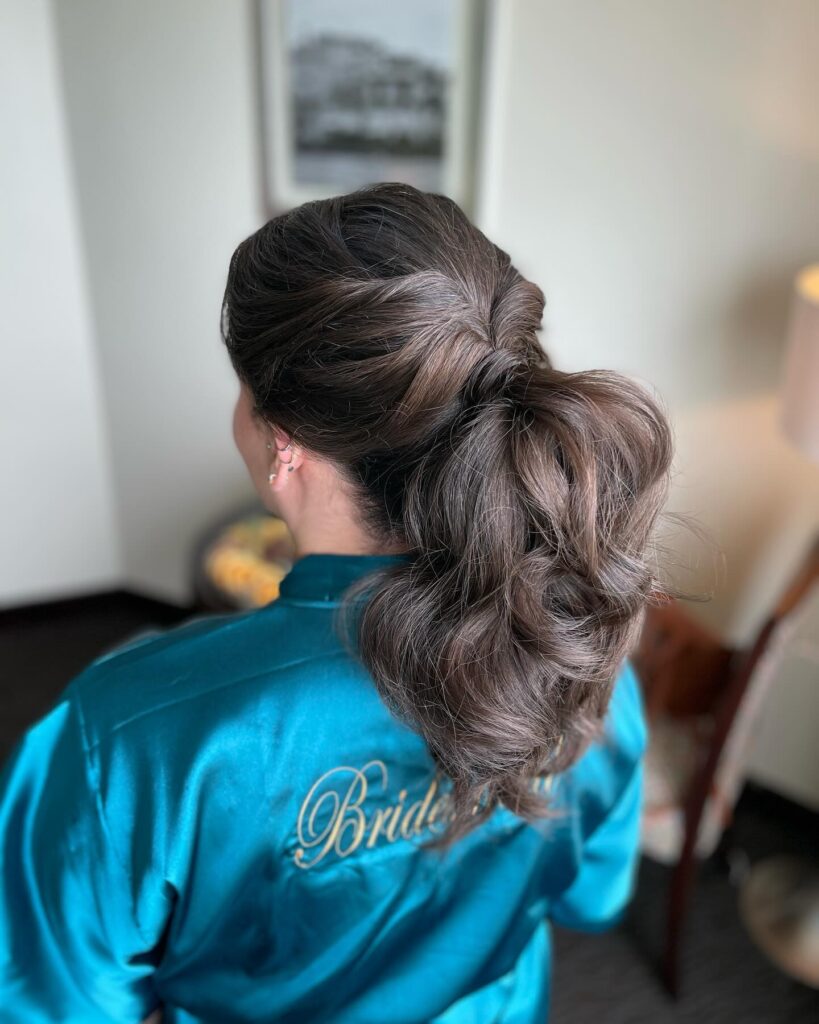 A woman from behind with a medium-length wavy brunette ponytail, featuring a twisted hair wrap at the base.