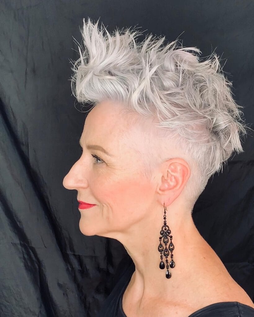 A woman in profile is showing off an icy white pixie cut with an undercut and tall, spiky, textured layers on top.