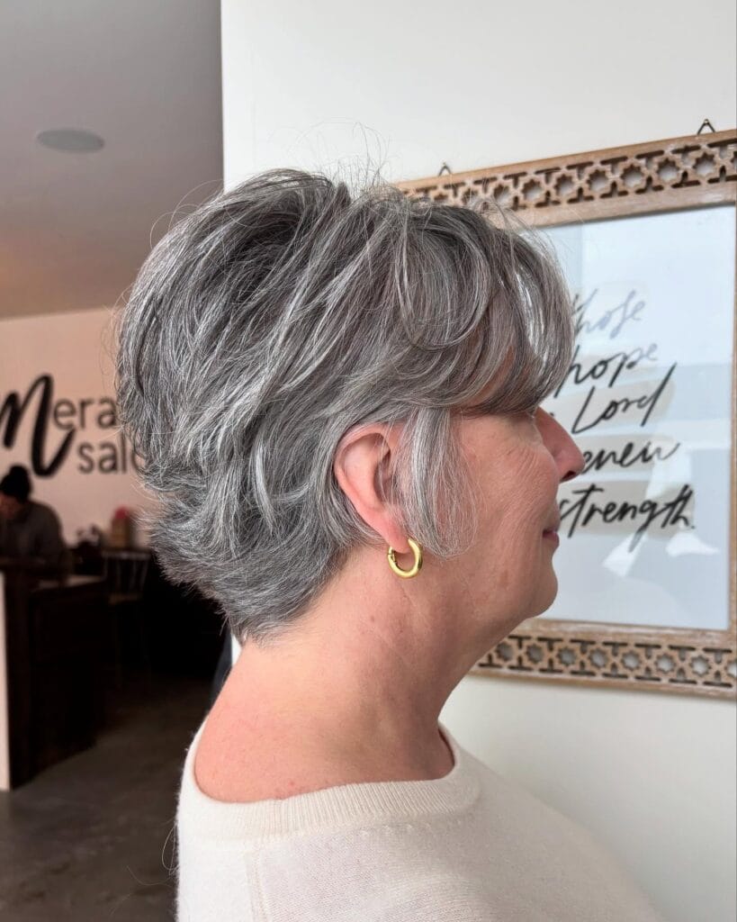A woman in profile wearing a voluminous salt-and-pepper short shag hairstyle with feathered layers and face-framing fringe.