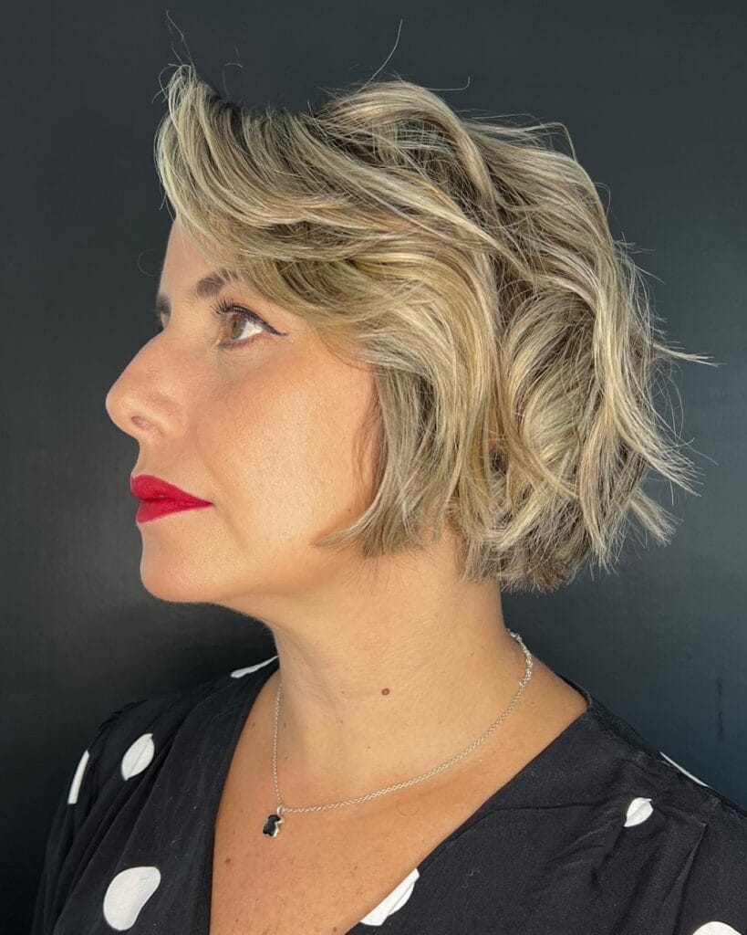 A woman in profile with a wavy ash blonde bob featuring voluminous sweeping layers and a side part.