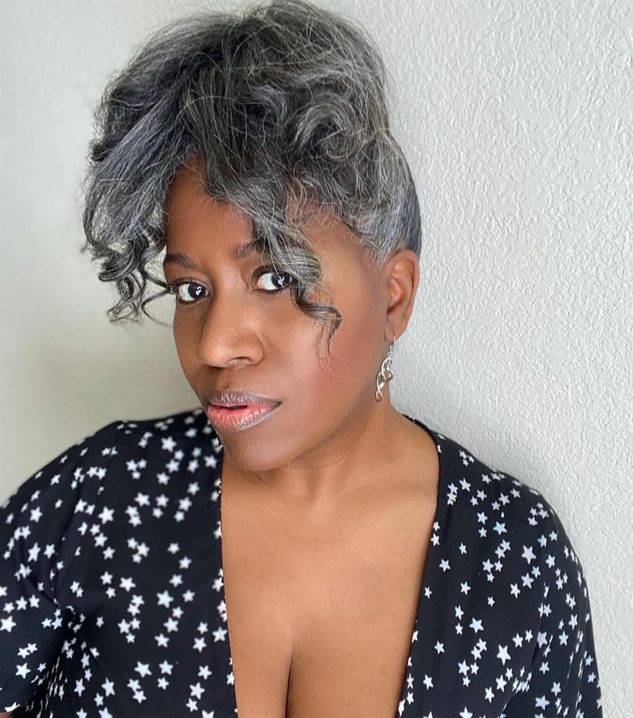 A woman with a voluminous curly salt-and-pepper hairstyle styled into a faux hawk with a sleek side.