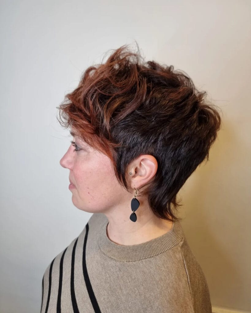 A woman in profile with a short shullet hairstyle featuring dark hair with auburn highlights and messy textured layers.