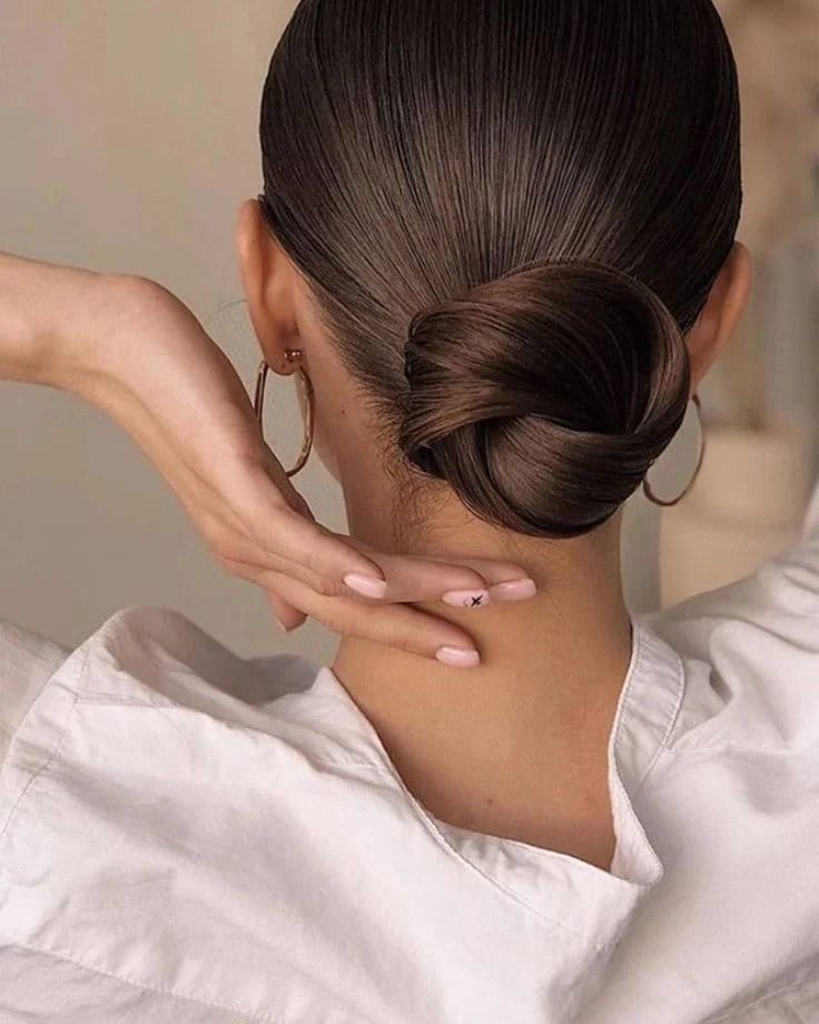 A back view of a woman with dark brown hair styled into a tight, shiny low bun at the neck.
