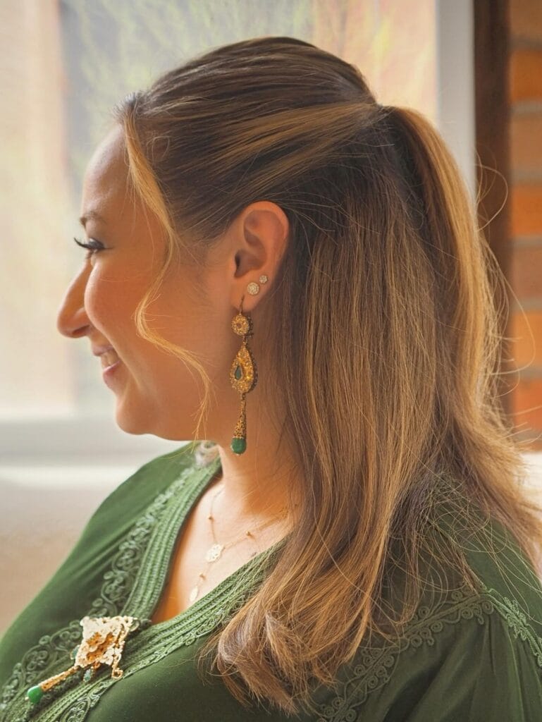 A woman in profile with honey-blonde hair styled in a half-updo with soft face-framing wavy strands.