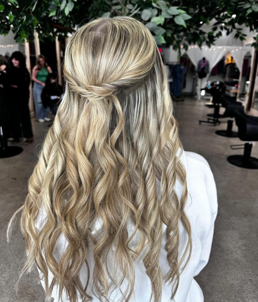 A back view of long blonde curly hair styled in a twisted half-updo.