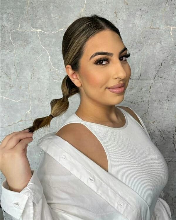 A young woman with a sleek center part wearing her blonde hair in a low bubble ponytail with multiple sections.