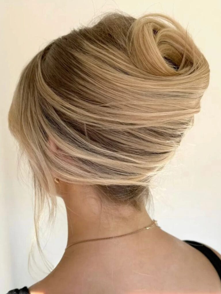 A close-up back view of a woman with blonde hair styled into a voluminous and smooth French twist updo.
