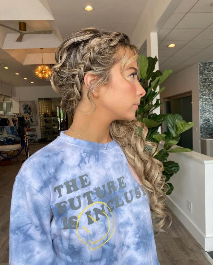 A young woman in profile featuring long, curly blonde hair with a thick side braid and a soft, face-framing fringe.