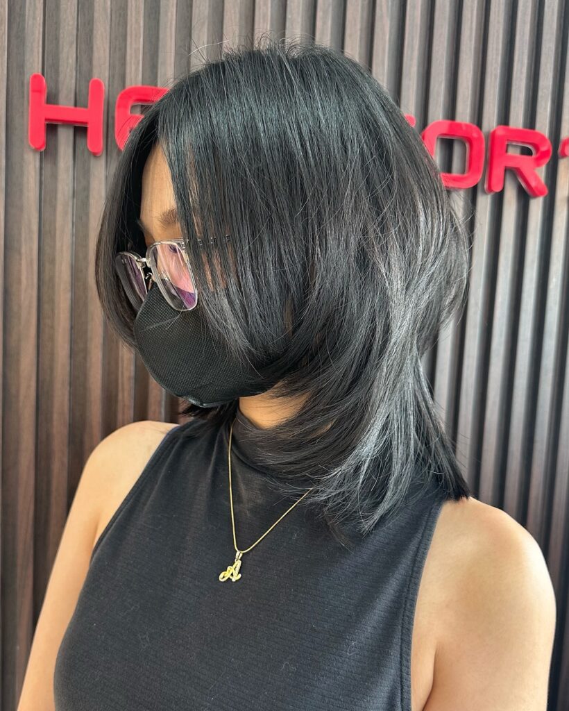 A woman from a side profile showing her shoulder-length, jet-black hair styled with heavy face-framing layers and a voluminous butterfly cut.