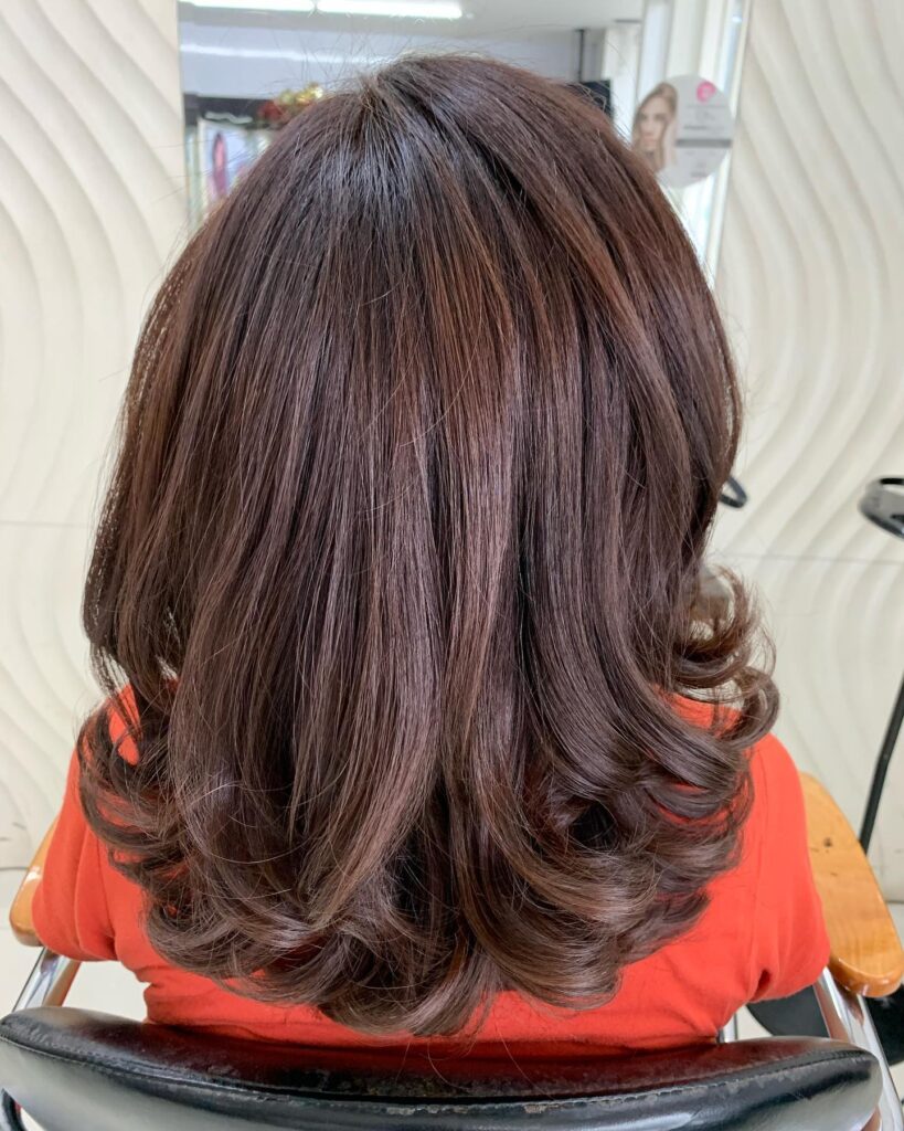 A back view of a woman with glossy auburn medium-length hair styled straight with voluminous curls flipped at the ends.