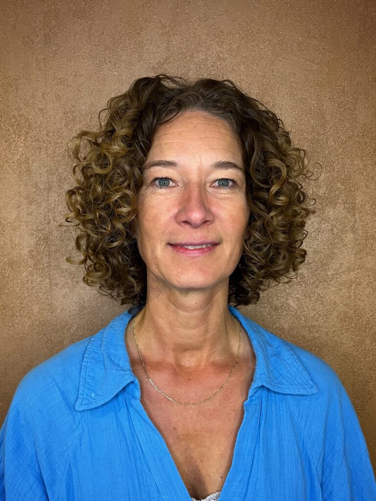 A woman with a shoulder-length curly bob featuring defined brown and caramel ringlets and a middle part.