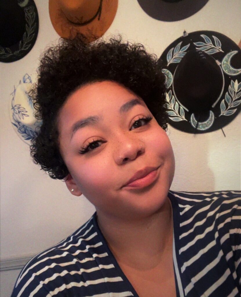 A woman with a short, voluminous, curly hairstyle featuring tight natural black coils concentrated on top with shorter sides.