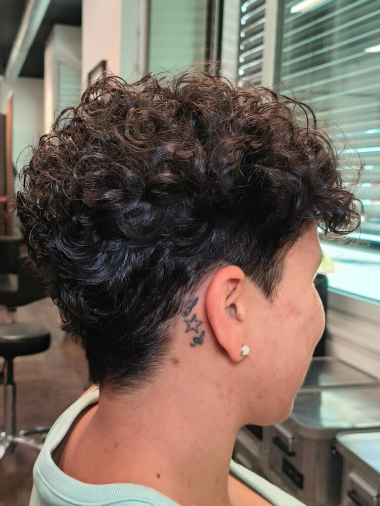 A woman viewed from the side with a short tapered curly pixie cut in a dark brown color.