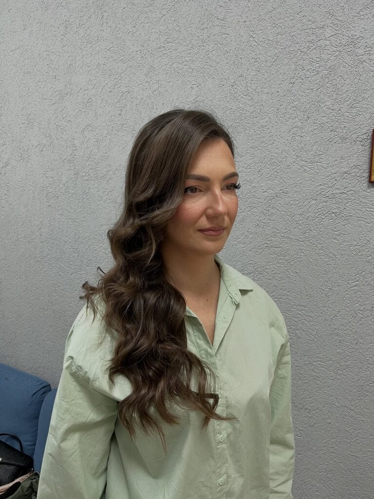 Long light brown wavy hair styled to one side with soft flowing layers.