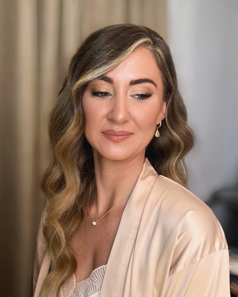 Long brown wavy hair with a side part and soft glam waves.